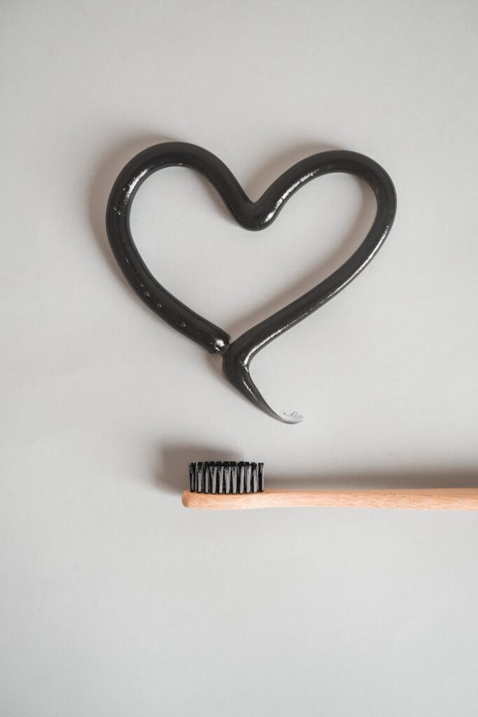 A wooden toothbrush with black bristles and heart-shaped charcoal toothpaste on a white background.
